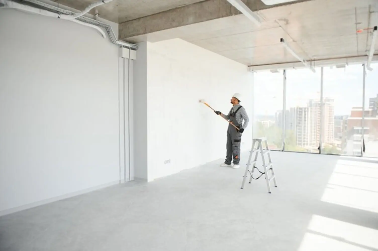 Commercial painter rolling a fresh coat on a cleared office wall, showing a work area prepared using a commercial painting project checklist for property managers.