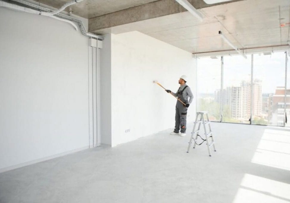 Commercial painter rolling a fresh coat on a cleared office wall, showing a work area prepared using a commercial painting project checklist for property managers.